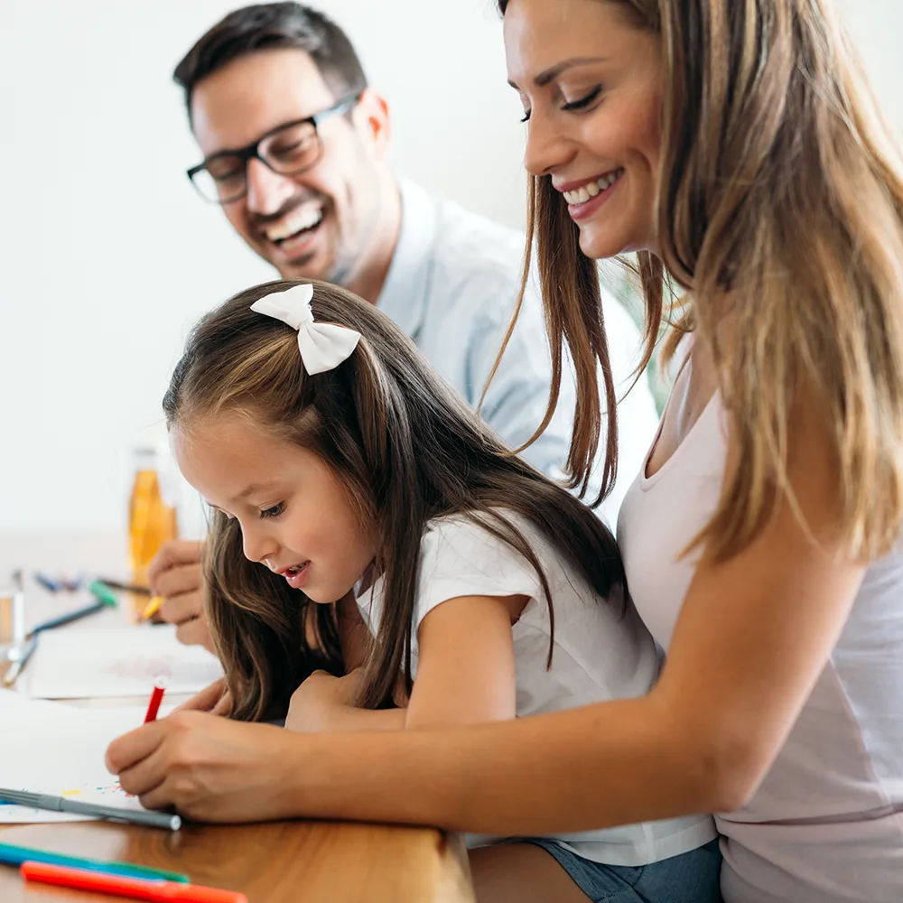 A laughing mother and father helping their child write in a book at a Peace of Mind daycare