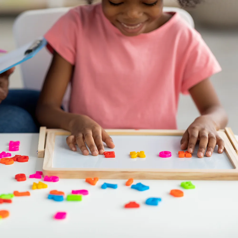 A child using magnetized colorful letters to spell HOME at a Peace of Mind daycare