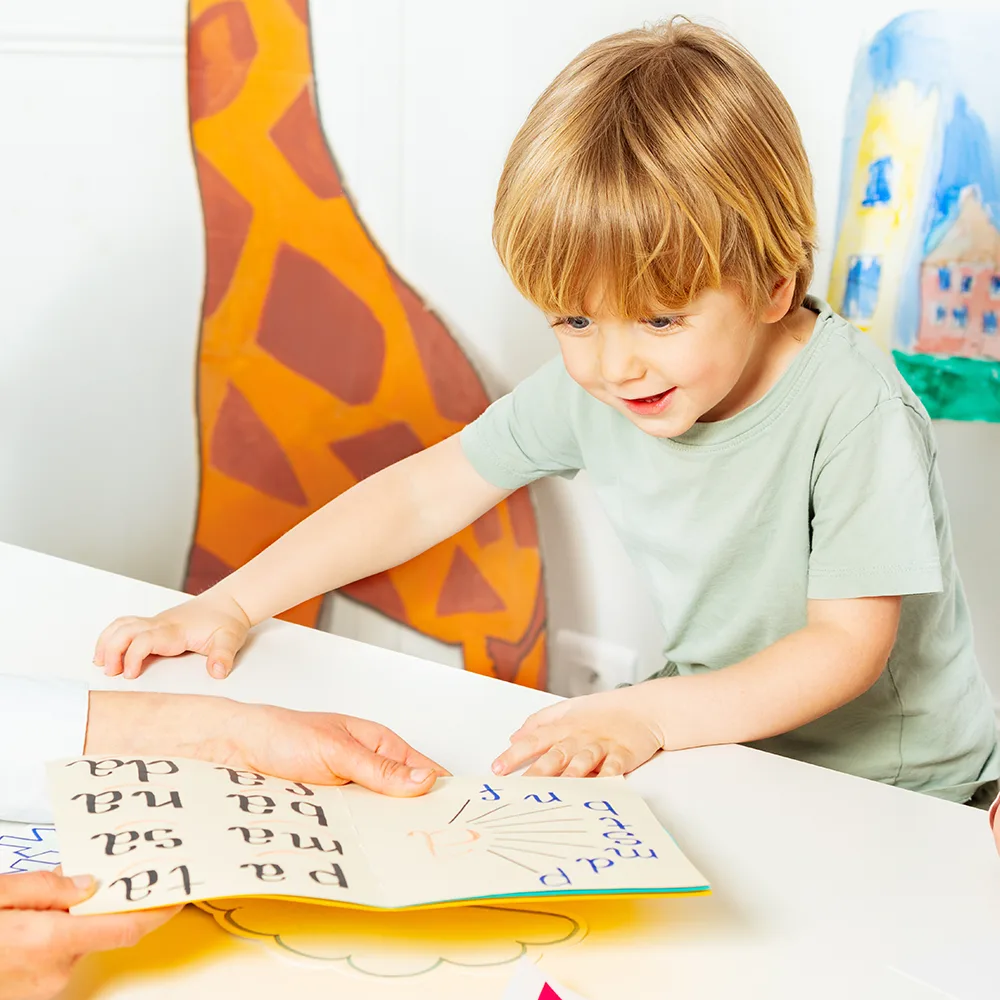 A child smiling and looking at a school book at a Peace of Mind daycare