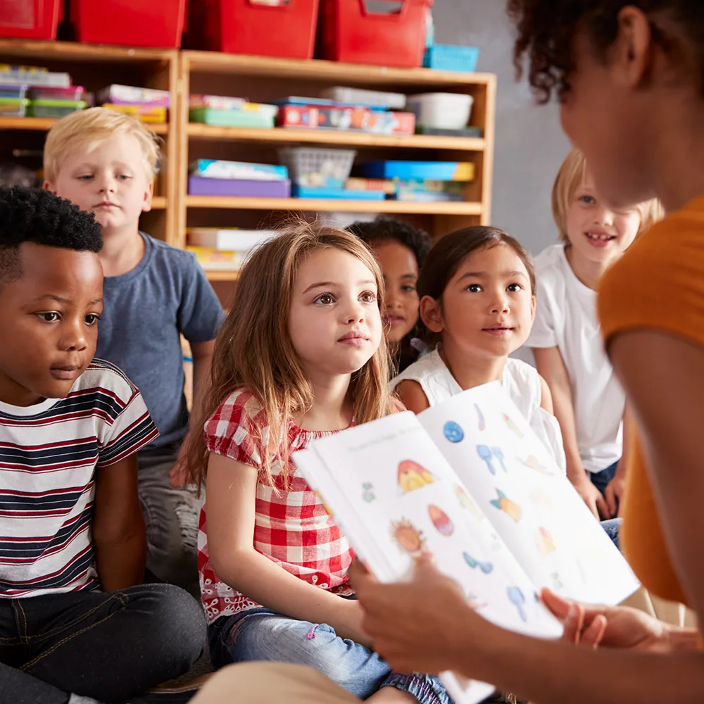 Children listening to a teacher read from a picture book at a Peace of Mind daycare