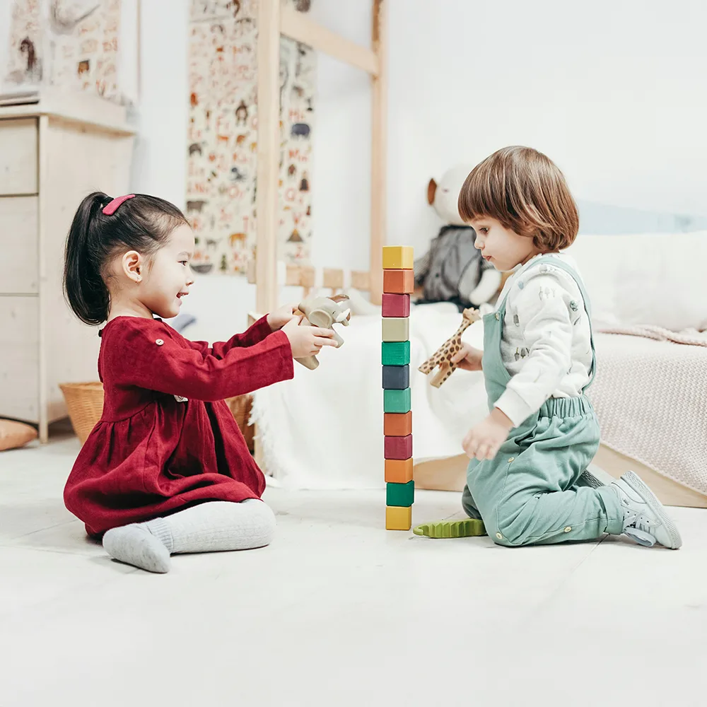 Two children stacking colorful blocks on a floor at Peace of Mind daycare