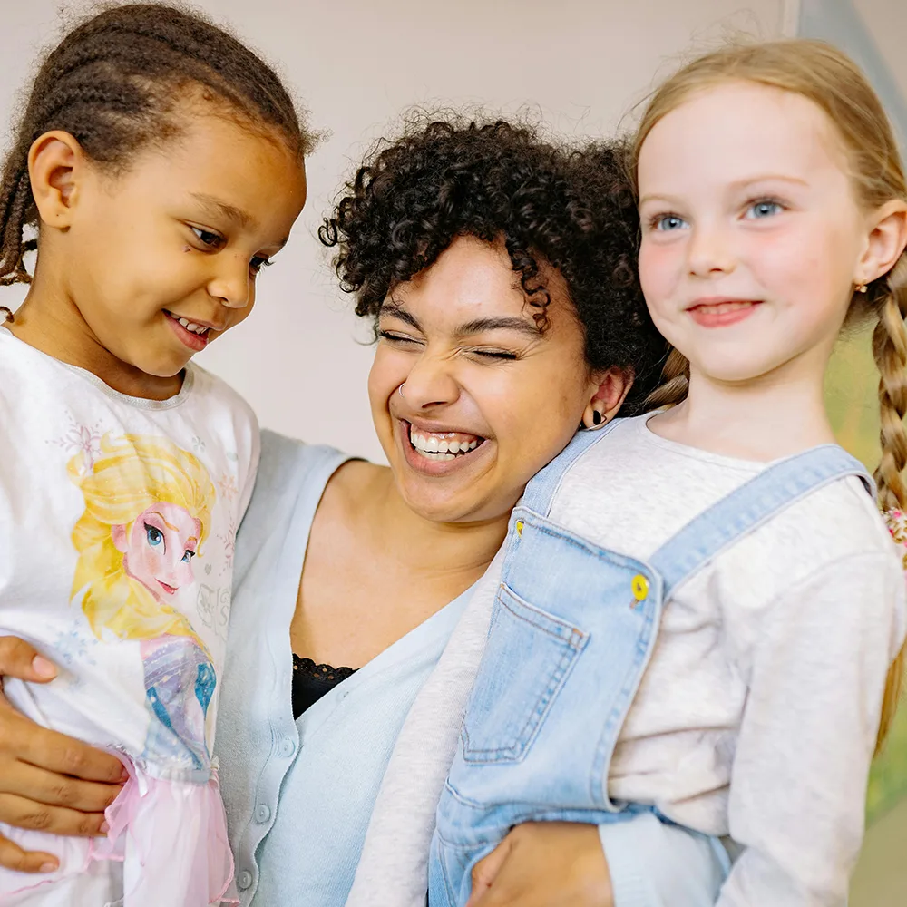 An adult hugging two children and smiling at a Peace of Mind daycare