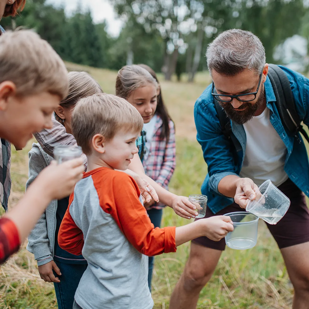 An adult playing with kids and glasses of water outside of a Peace of Mind daycare